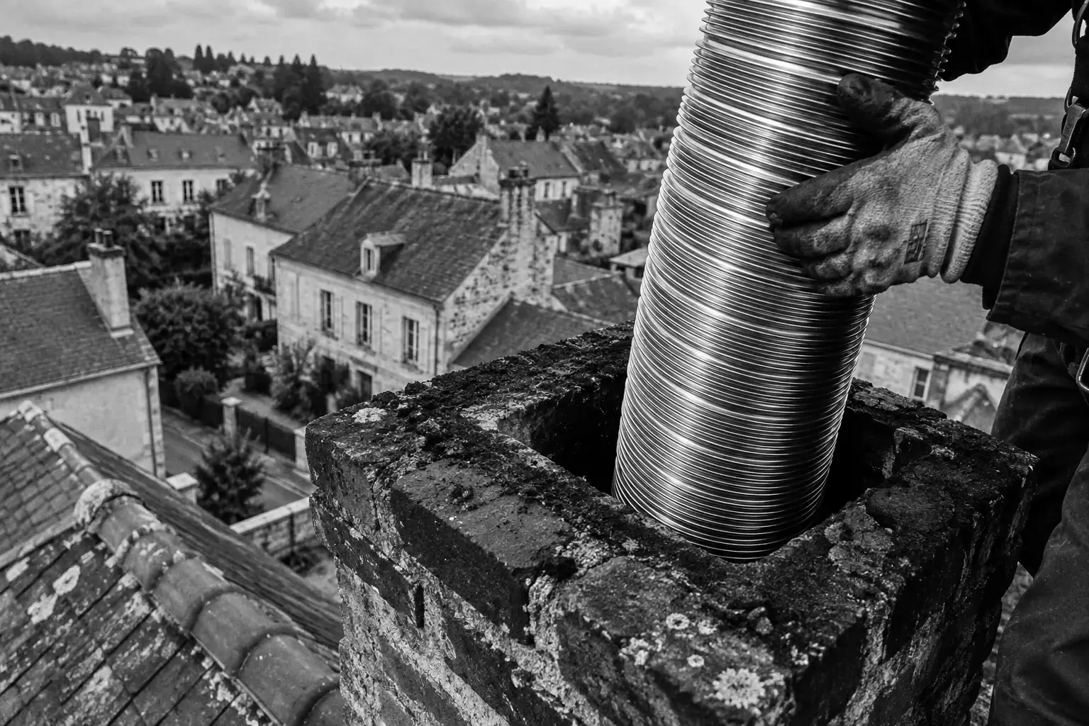 Conduit de tubage inox glissé dans une souche de cheminée en brique, au-dessus des toits